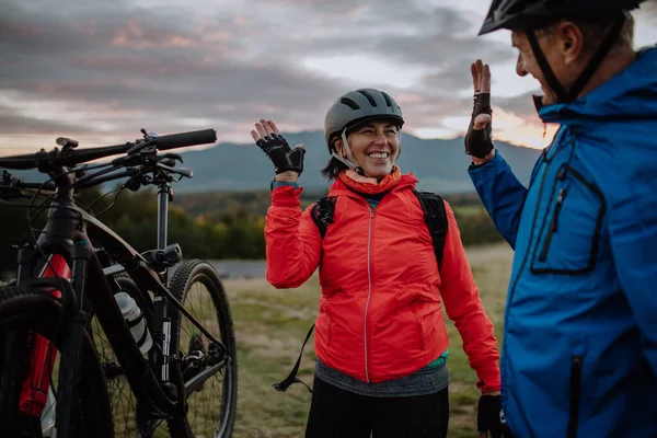 Senior pár bikers high fiving outdoors in forest in autumn day. — Stock fotografie