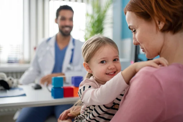 Little girl with her mother at doctors office on consultation, looking at camera. — Stock Photo, Image