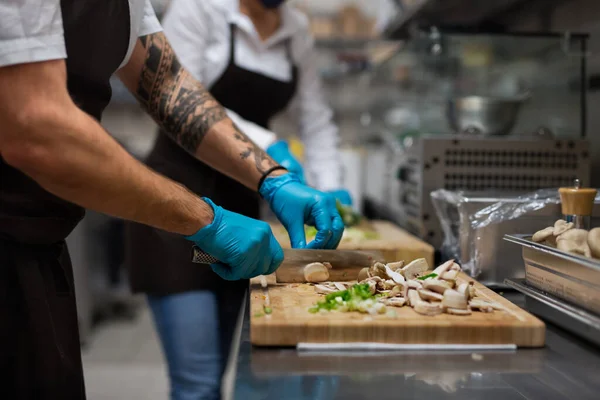 Cuoco irriconoscibile con guanti che tagliano verdure al chiuso in cucina ristorante. — Foto Stock