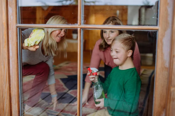 Pojke med Down syndrom med sin mor och mormor rengöring fönster hemma. — Stockfoto