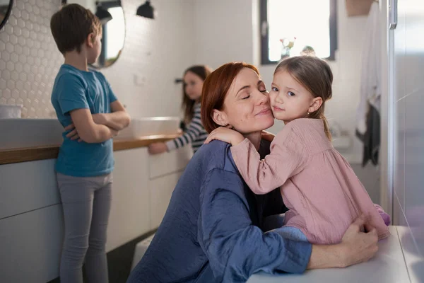 Mother of three little children hugging little daughter in bathroom at home. — Stock Photo, Image