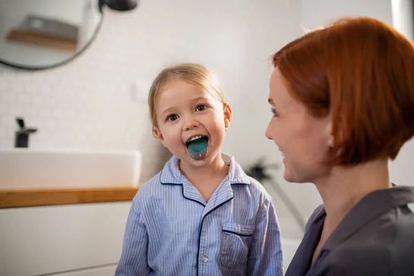 Маленька дівчинка приклеюється, показуючи свій синій язик матері у ванній вдома . — стокове фото