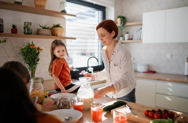 Mor till tre små barn förbereder frukost i köket hemma. — Stockfoto