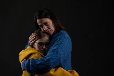 Üzücü anne, siyah arka planda Ukrayna ulusal renkleri giymiş kızına sarılıyor..