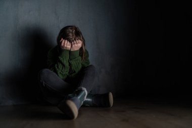 Üzgün küçük kız, karanlıkta yalnız, oturuyor ve yüzünü kapatıyor..