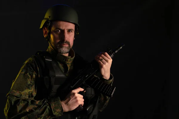 Askeri üniformalı ve miğferli bir asker siyah arka plandaki kameraya bakıyor.. — Stok fotoğraf