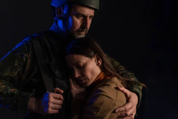 Sad woman saying good-bye to her military husband going to fight in war, on black background. — Stock Photo, Image