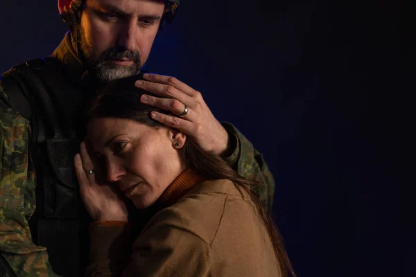 Sad woman hugging her military husband and saying-goodby to him before going to army on black backgound. — Stock Photo, Image