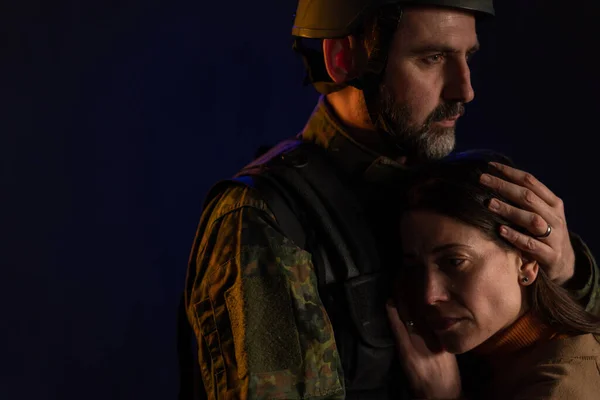 Traurige Frau umarmt ihren Militärgatten und verabschiedet sich von ihm, bevor sie auf schwarzem Rücken zur Armee geht. — Stockfoto