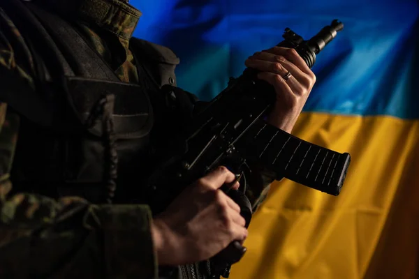 Зблизька солдат у військовій уніформі тримає зброю з прапором України на задньому плані.. — стокове фото