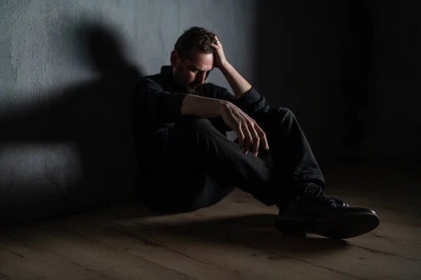 Droevige volwassen man, alleen in de duisternis, zittend en denkend. — Stockfoto