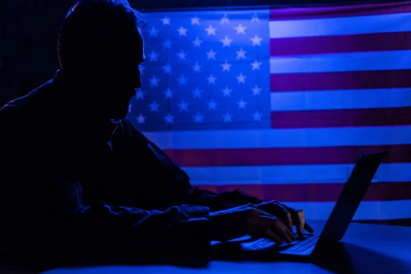 Hacker s notebookem a americkou vlajkou v pozadí. Koncept kybernetického útoku. — Stock fotografie