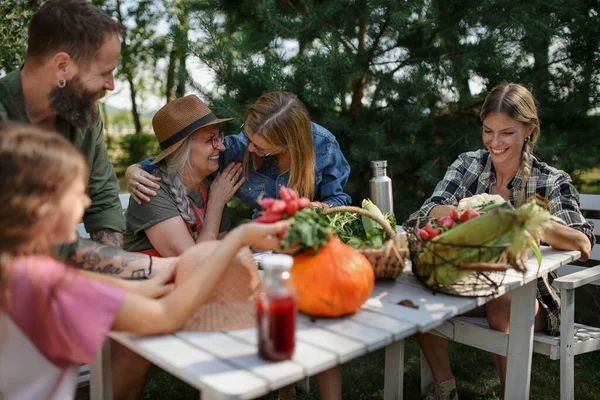 Keluarga petani yang bahagia duduk di meja dan melihat panen di luar di taman. — Stok Foto