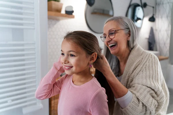 Senior grootmoeder en kleindochter staan binnen in de badkamer, dagelijkse routine concept. — Stockfoto