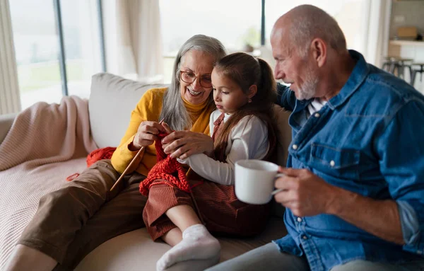 Menina sentada no sofá com seus avós e aprendendo a tricotar dentro de casa. — Fotografia de Stock