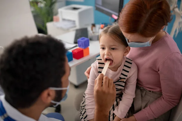 Ung manlig läkare kollar små flickor hals på sitt kontor. — Stockfoto