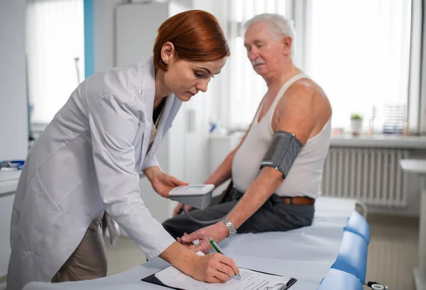 Medico femminile che misura la pressione sanguigna al paziente anziano nel suo ufficio. — Foto Stock