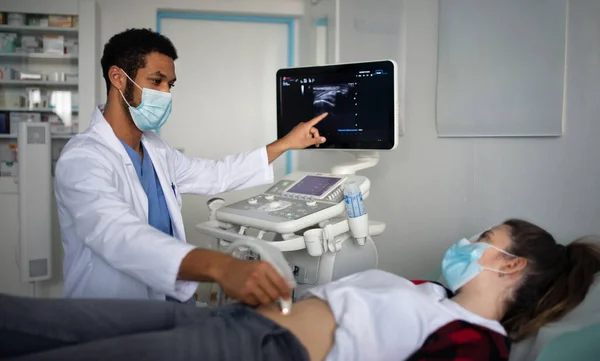 Jonge arts onderzoekt jonge vrouw met behulp van een echografie apparatuur in kliniek, coronavirus concept. — Stockfoto