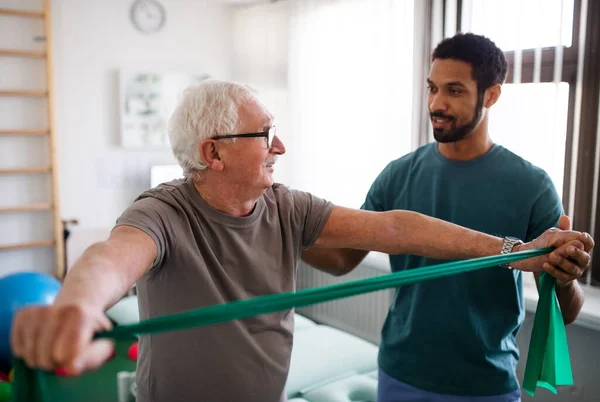Mladý fyzioterapeut cvičí se starším pacientem ve fyzikální místnosti — Stock fotografie