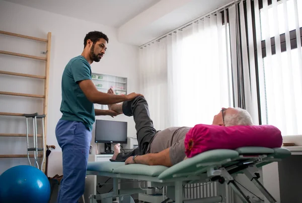 Fisioterapista che esercita con i pazienti anziani gamba in una stanza fisica. — Foto Stock
