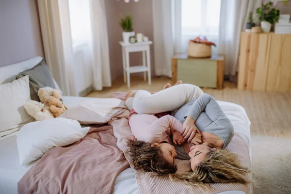 Felice madre con la sua piccola figlia sdraiata e guardarsi insieme sul letto a casa. — Foto Stock
