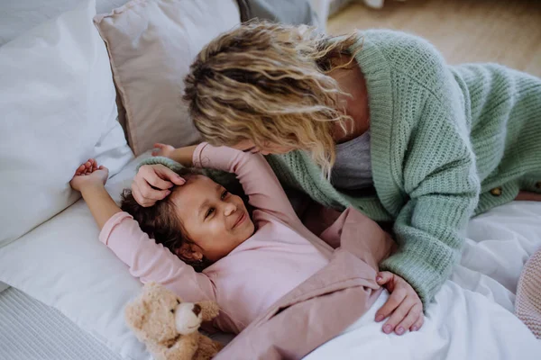 Glückliche Mutter streichelt ihre kleine Tochter, wenn sie morgens aufwacht. — Stockfoto