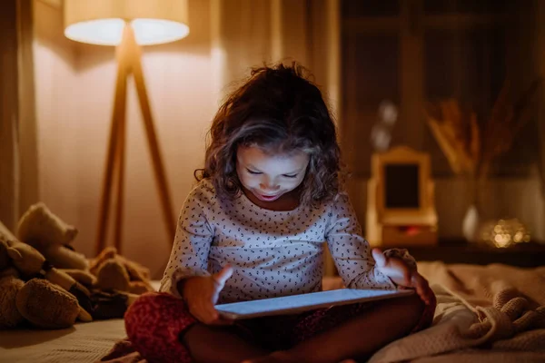 Feliz niña multirracial utilizando tableta en la cama por la noche en casa. — Foto de Stock