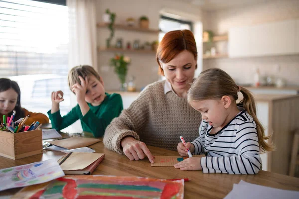Мати трьох маленьких дітей контролює їх при виконанні домашнього завдання вдома . — стокове фото