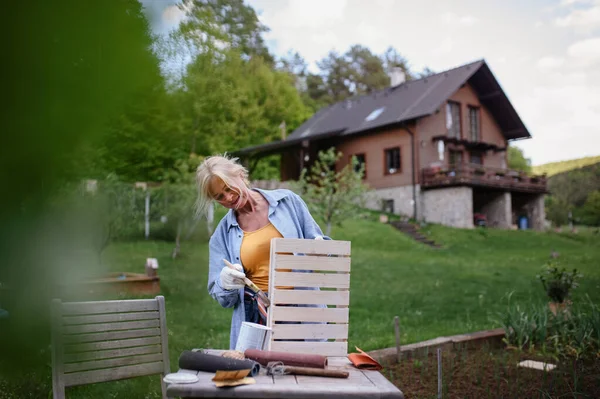 Mujer mayor con pincel impregnando cajón de madera al aire libre en el jardín. —  Fotos de Stock