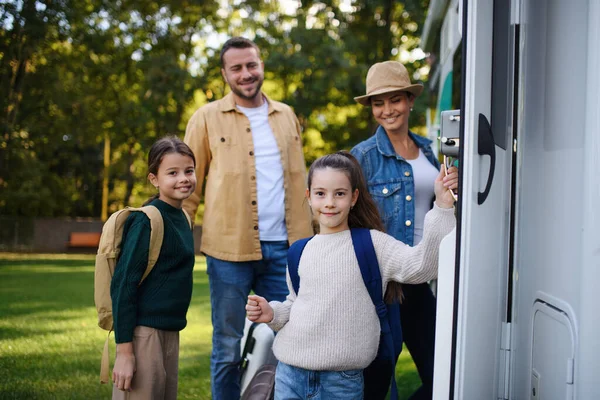 Happy young family with luggage looking at camera with camper at background outdoors in garden. — Stock Photo, Image