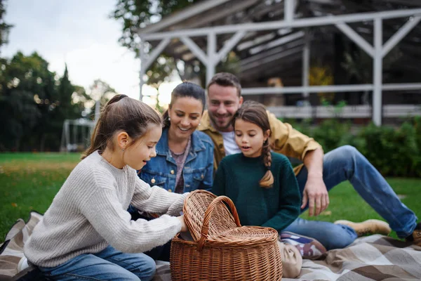 Счастливая молодая семья, сидящая на одеяле и уносящая пикник на улицу в районе ресторана. — стоковое фото