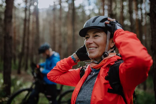 Senior couple bikers putting on cycling helmet outdoors in forest in autumn day. — Stock Photo, Image