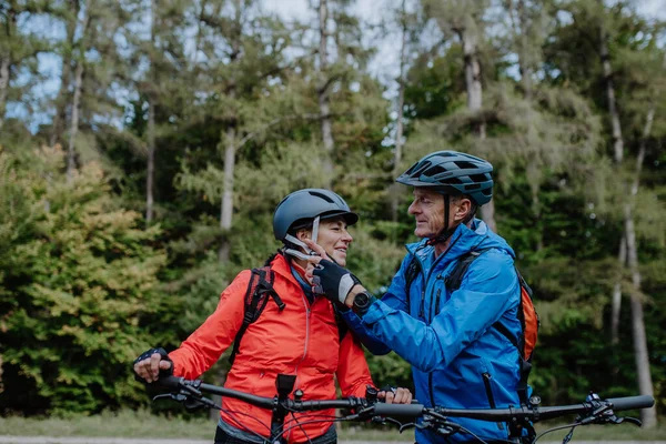 Starší pár cyklisté uvedení na cyklistické helmy venku v lese na podzim. — Stock fotografie