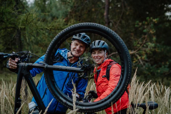 Aktives Seniorenpaar flickt im Herbst Fahrrad im Wald. — Stockfoto