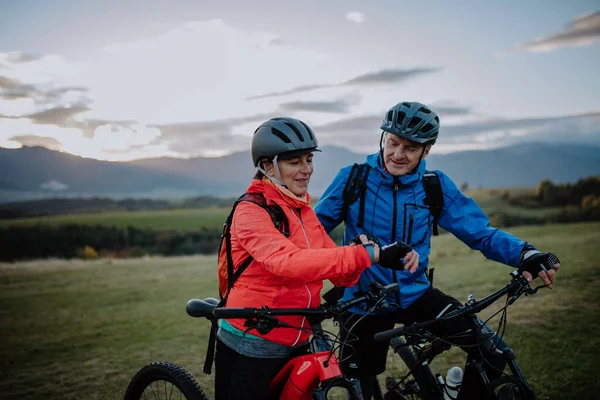 Senior paar bikers instellen smartwatch buiten in het bos in de herfst dag. — Stockfoto