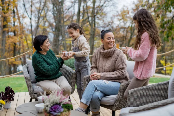 Dua saudara perempuan yang bahagia dengan ibu dan nenek duduk dan minum teh di luar ruangan di patio pada musim gugur. — Stok Foto