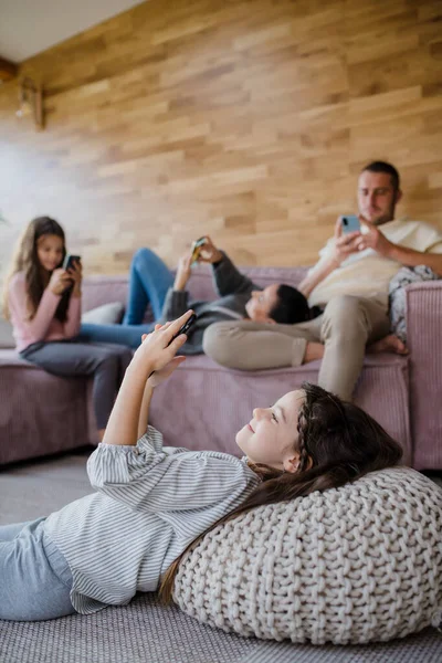 Familia con dos hijas pequeñas, todo el mundo está usando el teléfono móvil en la sala de estar. — Foto de Stock