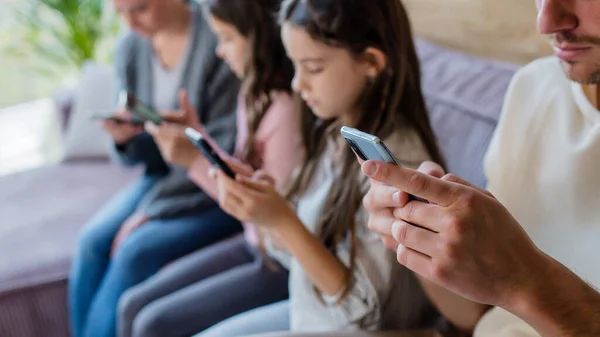 Familj med två små döttrar, alla använder mobiltelefon i vardagsrummet. — Stockfoto