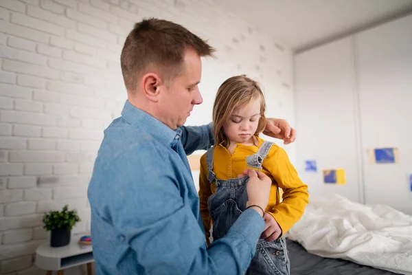 Vater hilft seiner kleinen Tochter mit Down-Syndrom, zu Hause Hosen zu tragen. — Stockfoto