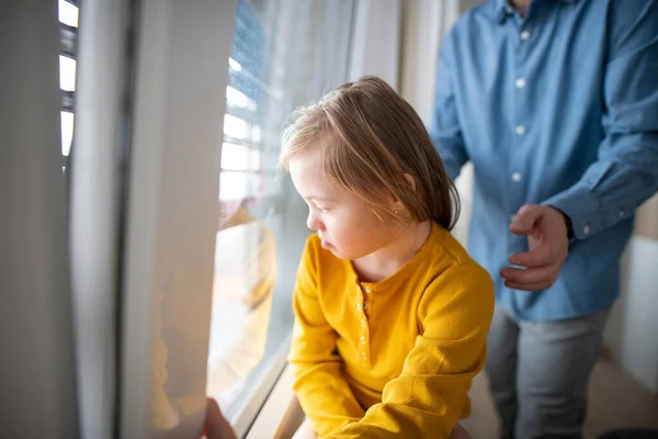 Down sendromlu üzgün küçük bir kız. Arka planda babasıyla pencereye bakıyor.. — Stok fotoğraf