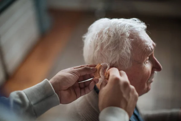 Zbliżenie opiekun mans ręka wkładanie aparat słuchowy w seniorów człowiek ucho. — Zdjęcie stockowe