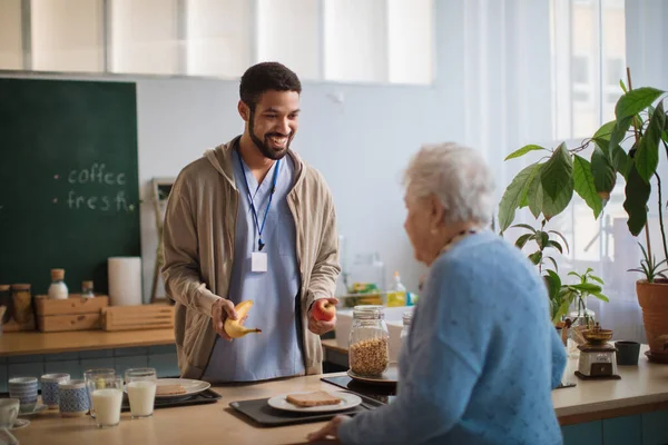 Cuidador joven que sirve el desayuno a una mujer anciana en el centro de atención en el hogar de ancianos. — Foto de Stock