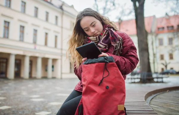 Giovane donna con sindrome di Down seduta sulla panchina e con tablet in città in inverno — Foto Stock