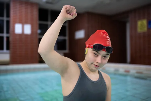 Young woman with Down syndrome inm swimming pool raising arm and looking at camera