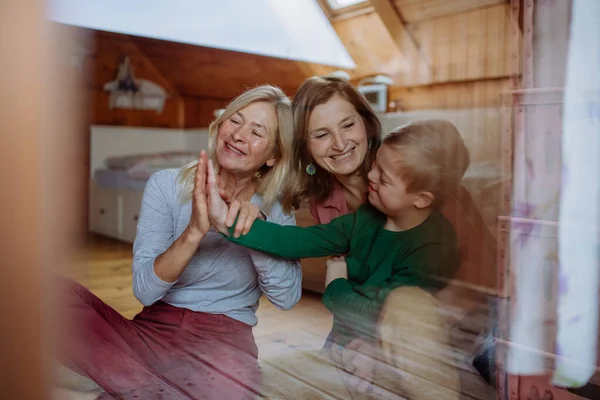 Jongen met Down syndroom met zijn moeder en grootmoeder zitten en kijken door het raam thuis. — Stockfoto