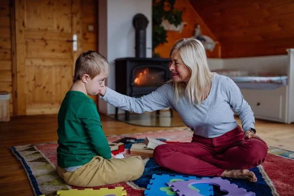 Boy with Down syndroom zitten op de vloer en spelen met zijn grootmoeder thuis — Stockfoto