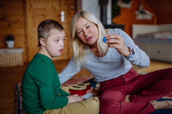 Boy with Down syndroom zitten op de vloer en spelen met zijn grootmoeder thuis — Stockfoto