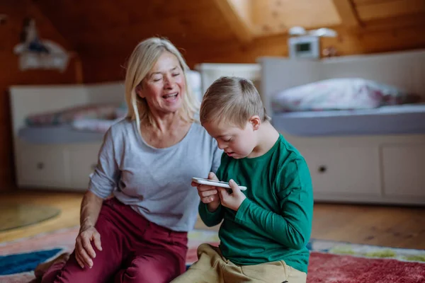 Kind met Down syndroom zitten op de vloer en het gebruik van tablet met oma thuis. — Stockfoto