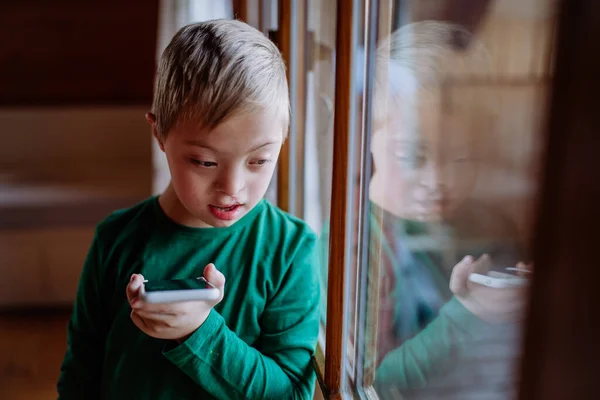 Sorglig liten pojke med Down syndrom med hjälp av smartphone hemma — Stockfoto