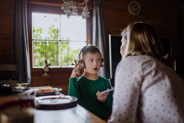 Niño con síndrome de Down con su madre almorzando y usando smartphone en casa — Foto de Stock